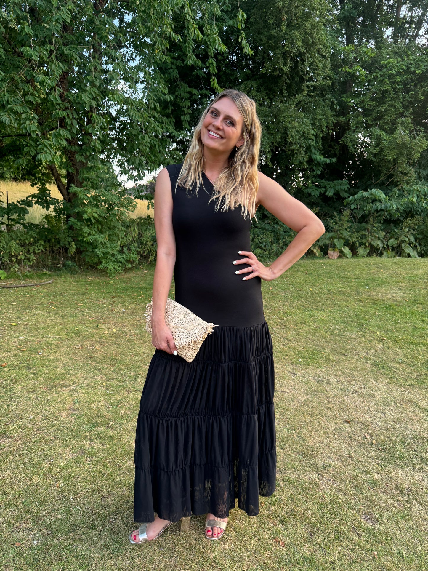 Woman in a black dress standing on grass with trees in the background wearing large sized womens shoes