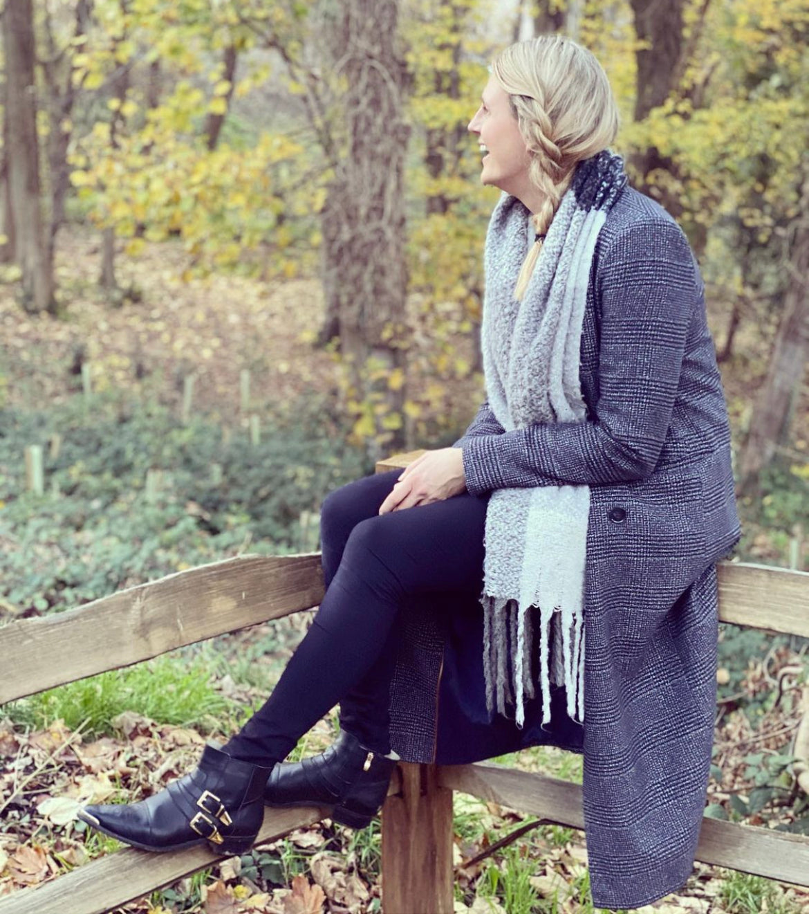 The Otto and Ivy black Tilly Boot, a western style ankle boot for tall women with large feet, featuring gold buckles and hardware, worn with a coat, black trousers and a scarf