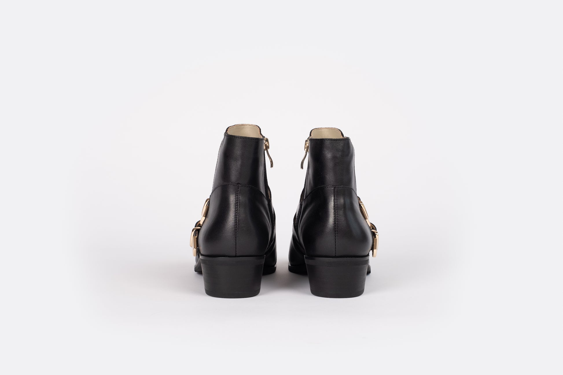 A back profile of the Otto + Ivy black Tilly Boot, a western style ankle boot for tall women with large feet, featuring gold buckles and hardware.